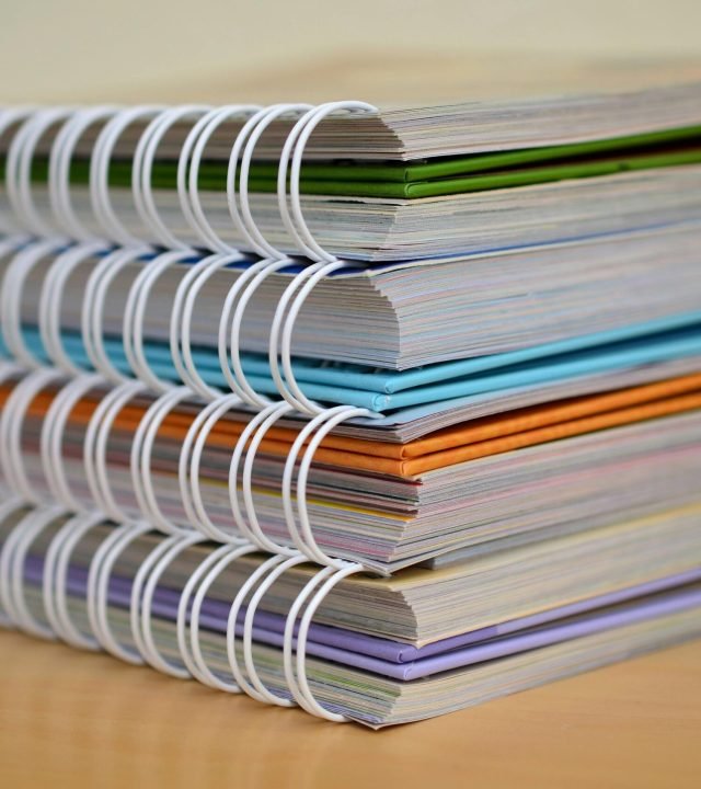 A colorful stack of spiral-bound notebooks neatly placed on a wooden desk. Ideal for educational themes.